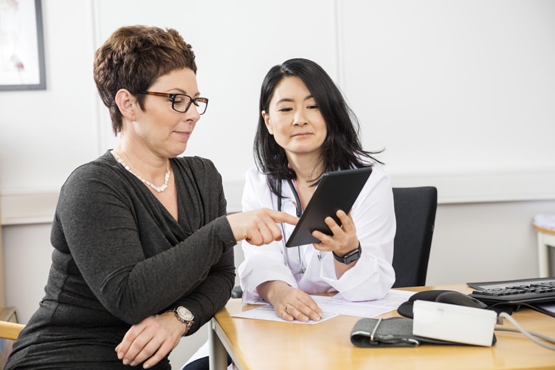 Woman interacting with tablet being held by her doctor.